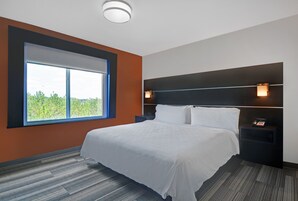 A modern hotel room with a large window, a neatly made bed, a nightstand with a phone, and a wall-mounted light fixture.