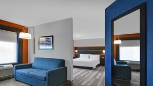 A hotel room with a blue sofa, a bed with white linens, a large mirror, and a framed picture on the wall. - Holiday Inn Express Atmore by IHG (Atmore)