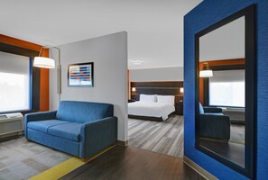 Ein Hotelzimmer mit einem blauen Sofa, einem Bett mit weißen Leinentüchern, einem großen Spiegel und einem gerahmten Bild an der Wand.
