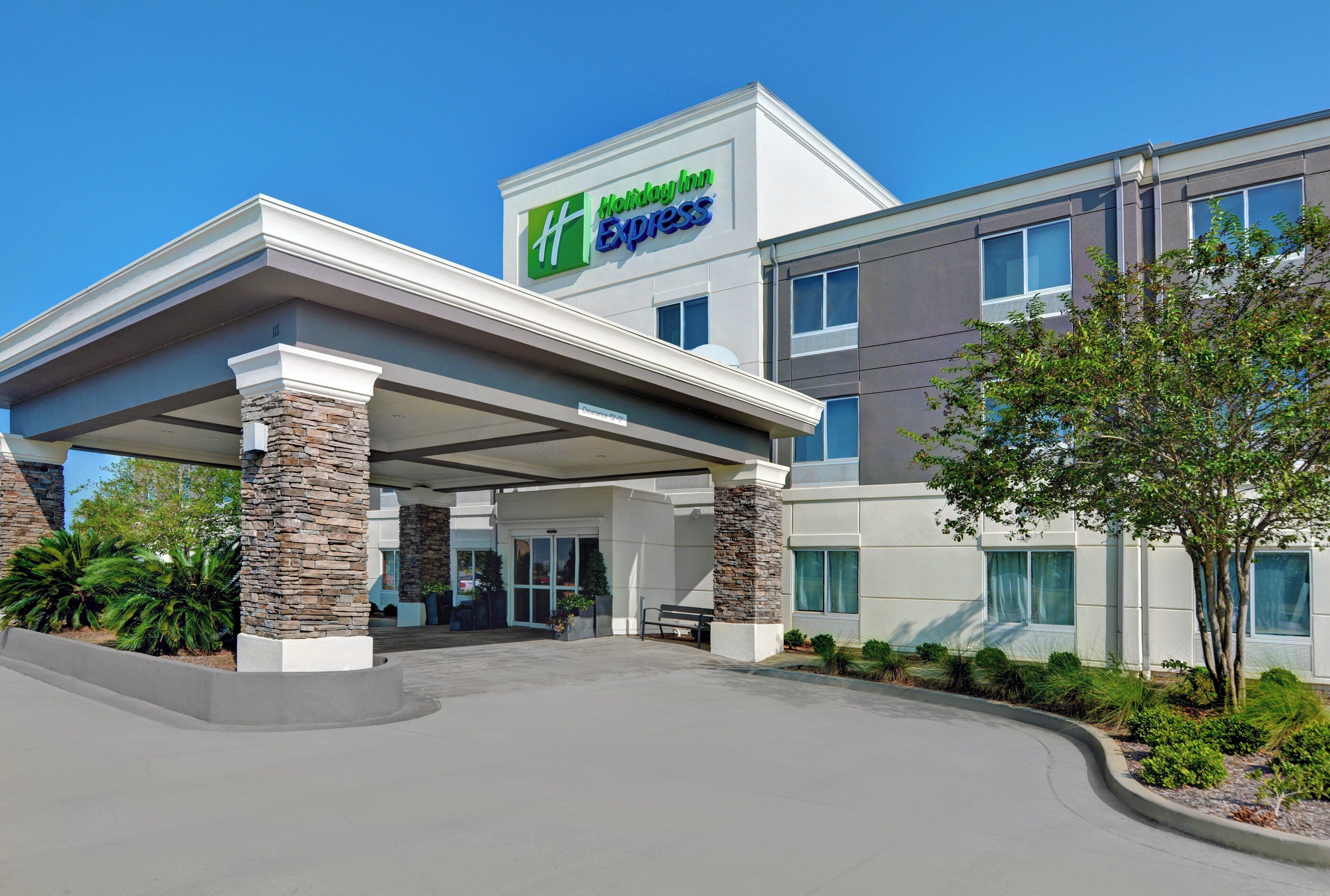 A Holiday Inn Express building with a covered entrance, stone pillars, and a clear sky.
