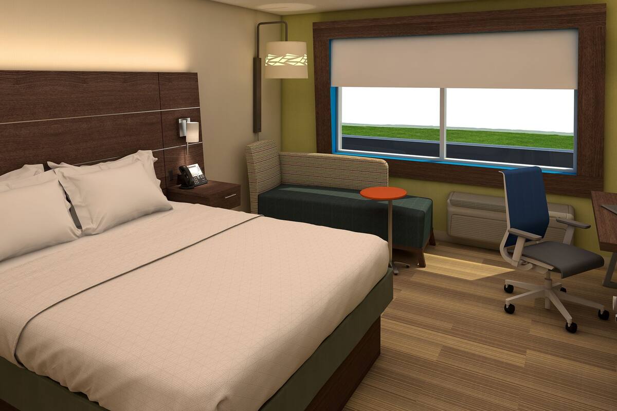A hotel room with a large bed, a desk, a chair, a lamp, and a window with a view of the sky.