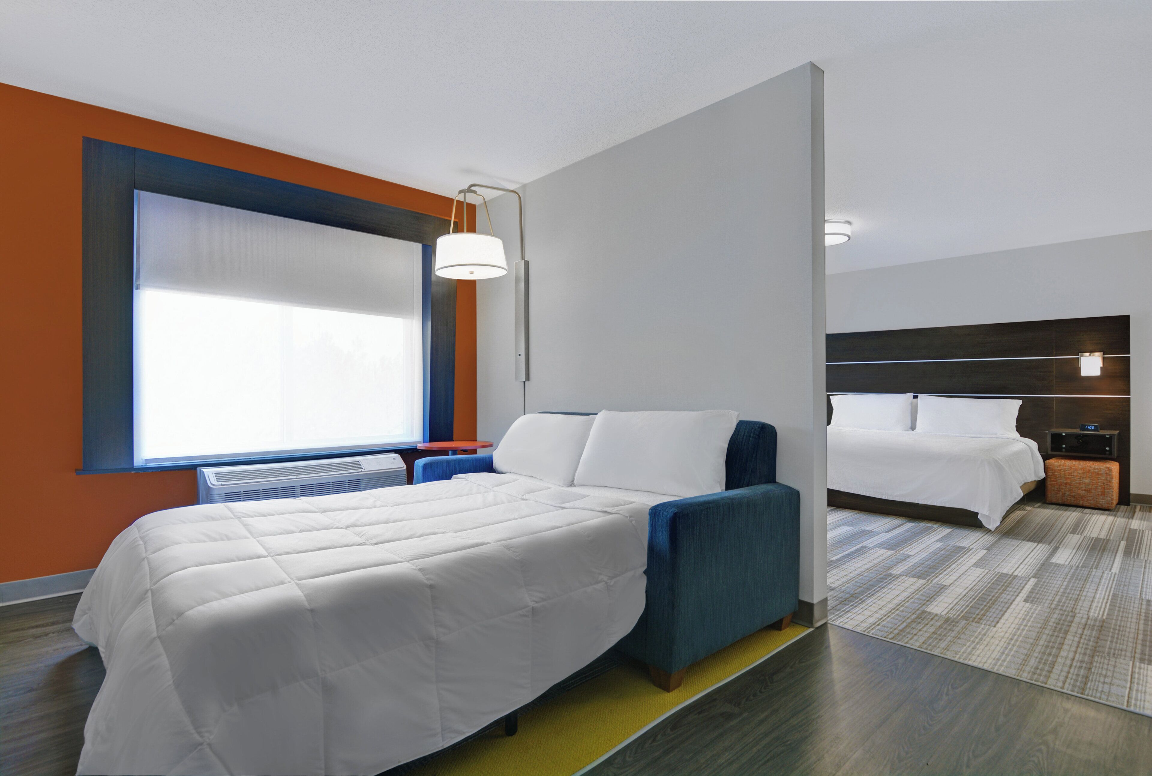 A hotel room with a large bed, a smaller bed, a desk, and a window.