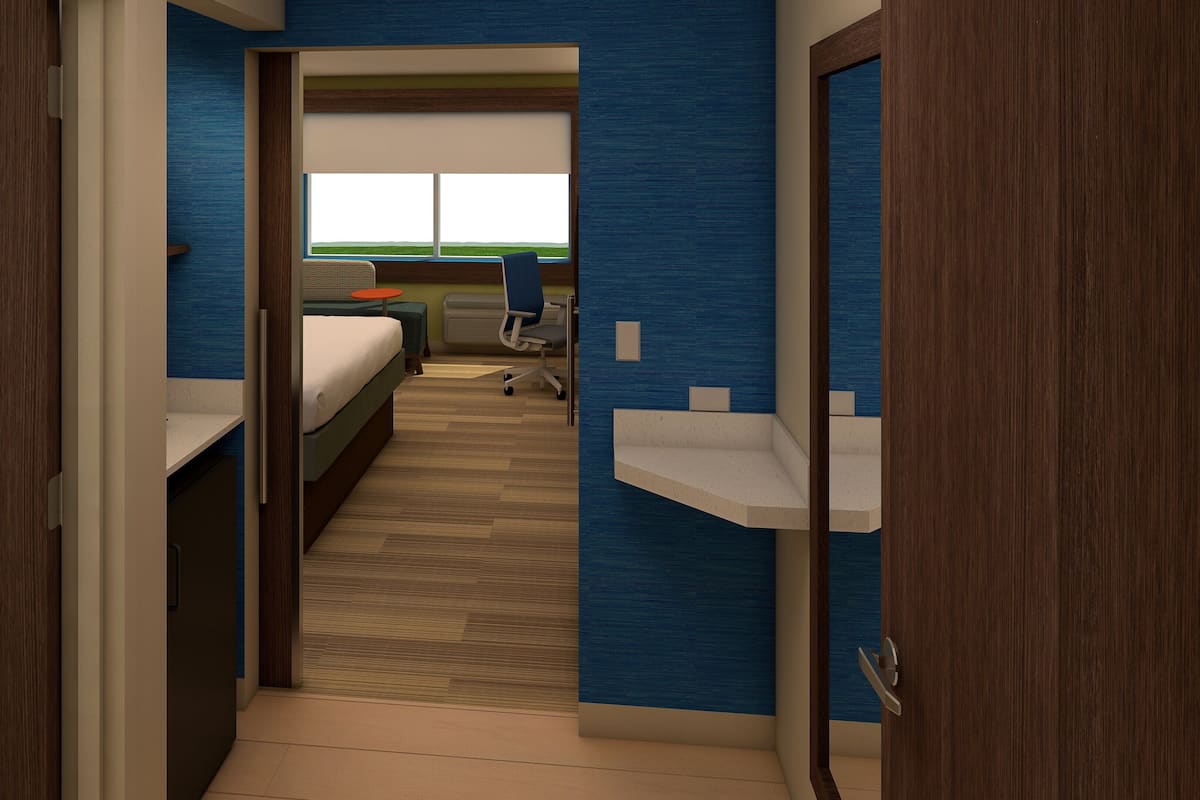 A narrow hallway with a bed, a desk, and a chair in the background.