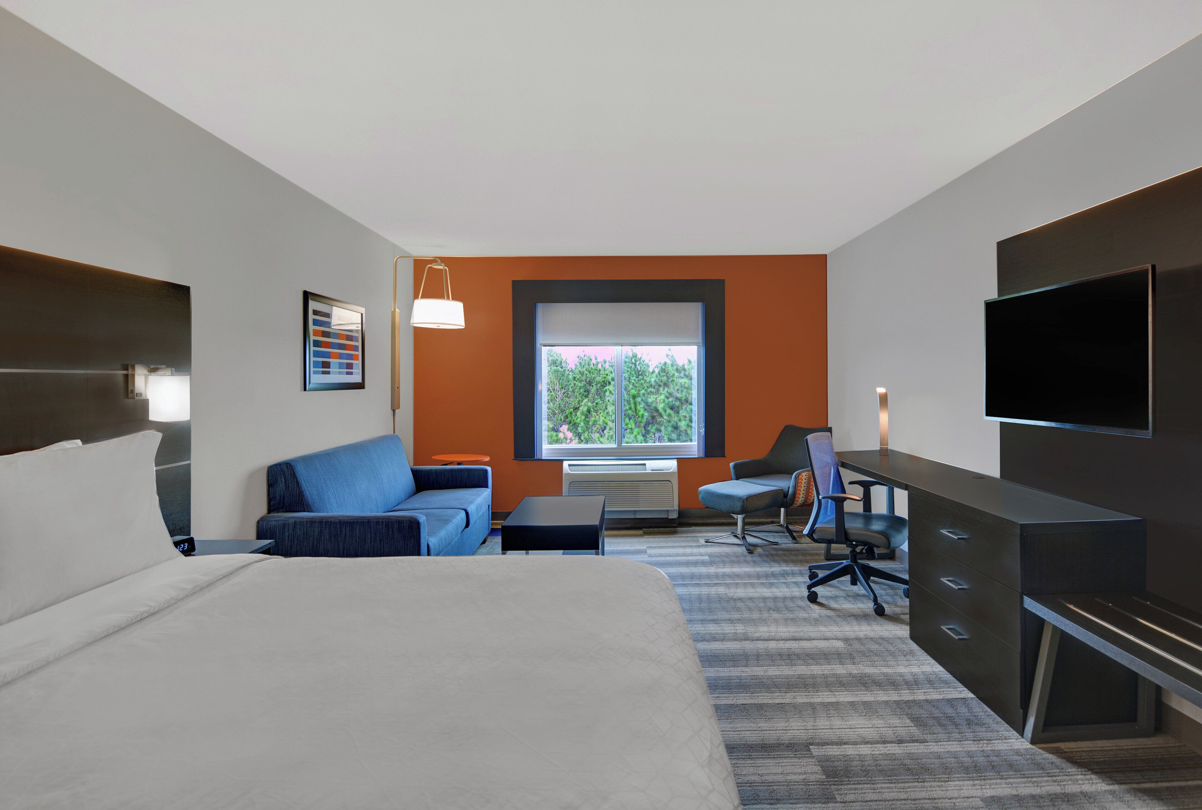 A hotel room with a large bed, a desk, a chair, and a TV.