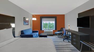 A hotel room with a large bed, a desk, a chair, and a TV.