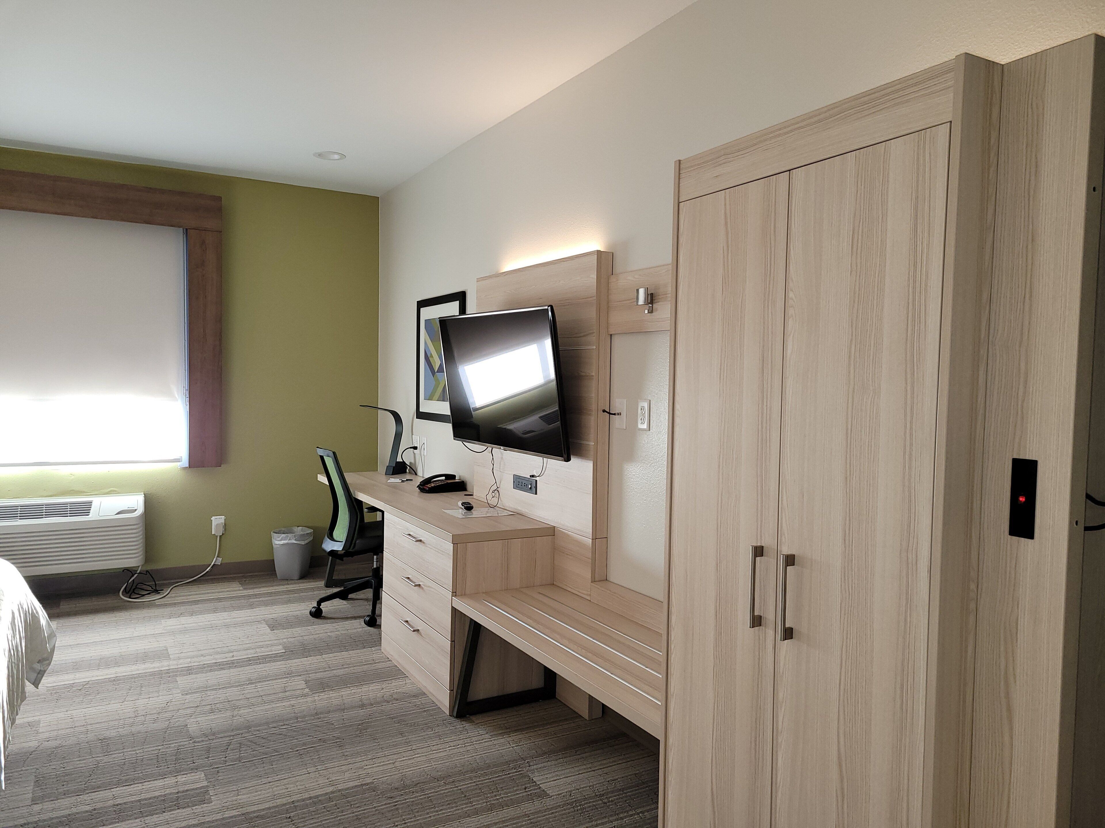 Ein Hotelzimmer mit einem Bett, einem Schreibtisch mit Computer, einem Fernseher und einem Kleiderschrank.