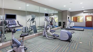 Un gimnasio con equipo de ejercicio, un espejo grande y suelo alfombrado.