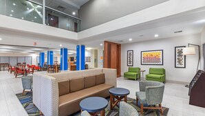 Un vestíbulo espacioso con techo alto, una zona de estar central con sofá y sillones, una escalera y obras de arte en las paredes.