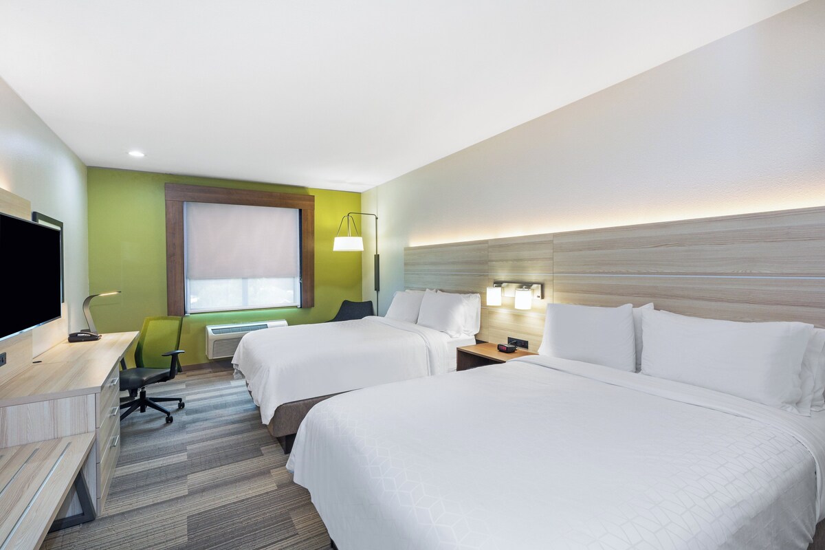 A hotel room with two beds, a desk, a chair, and a TV.