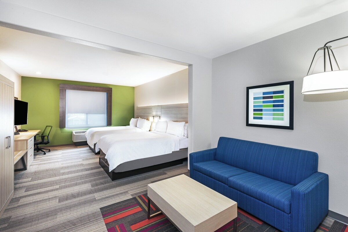 A hotel room with a bed, a blue sofa, a desk with a chair, and a television.