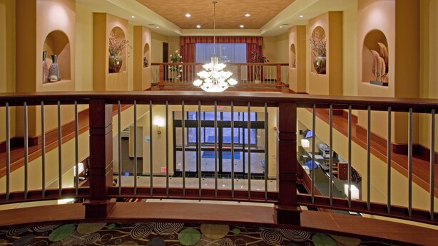 Vestíbulo de hotel con una escalera central, un candelabro y jarrones decorativos.