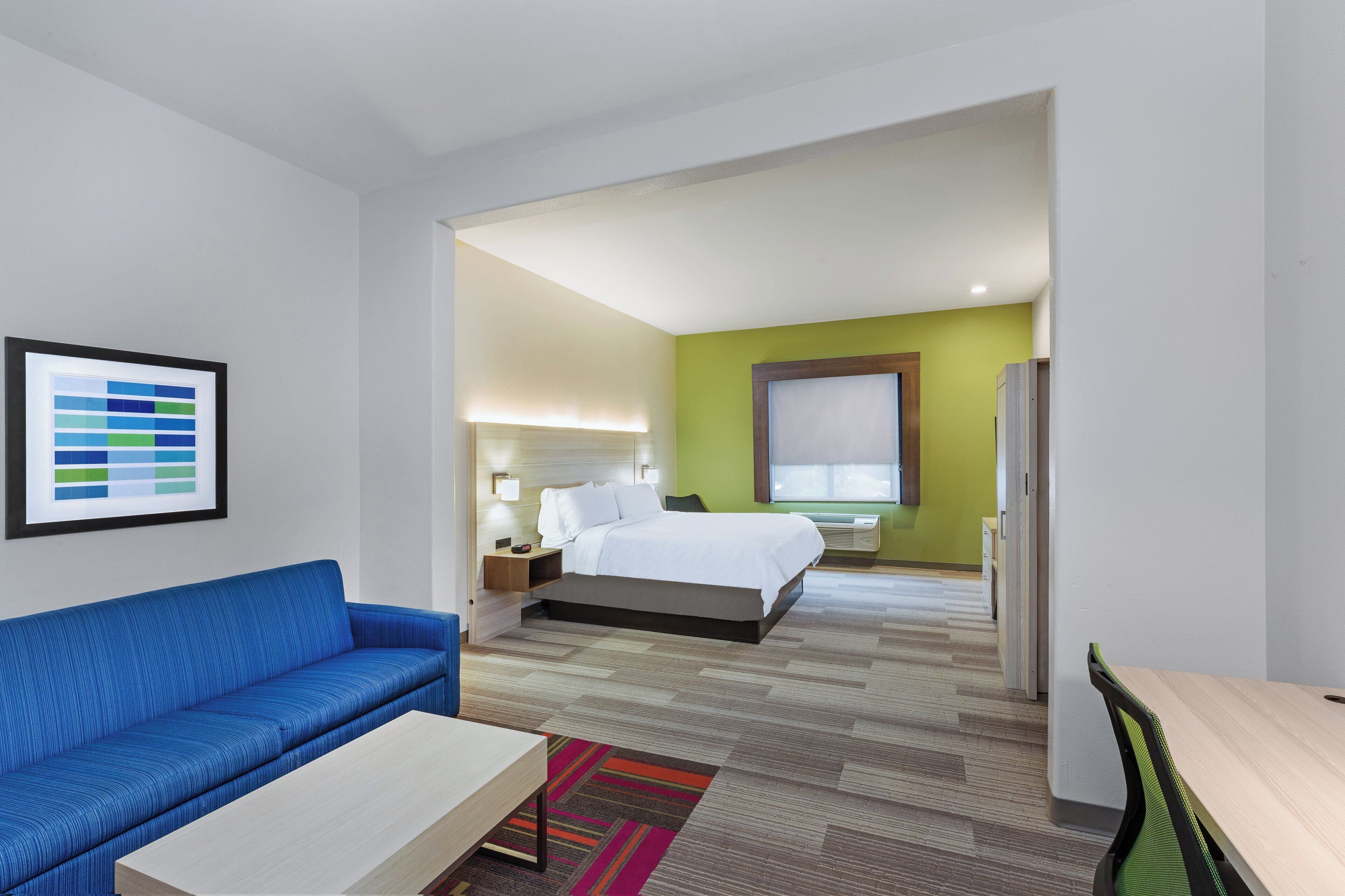 A hotel room with a bed, a blue sofa, a small table, and a colorful rug.