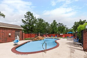 A swimming pool with a brick border, lounge chairs, and a red fence.