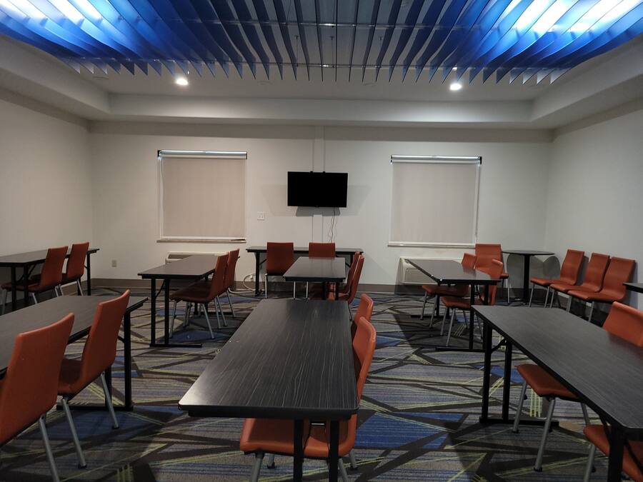 A conference room with tables and chairs, a flat-screen TV, and windows with blinds.