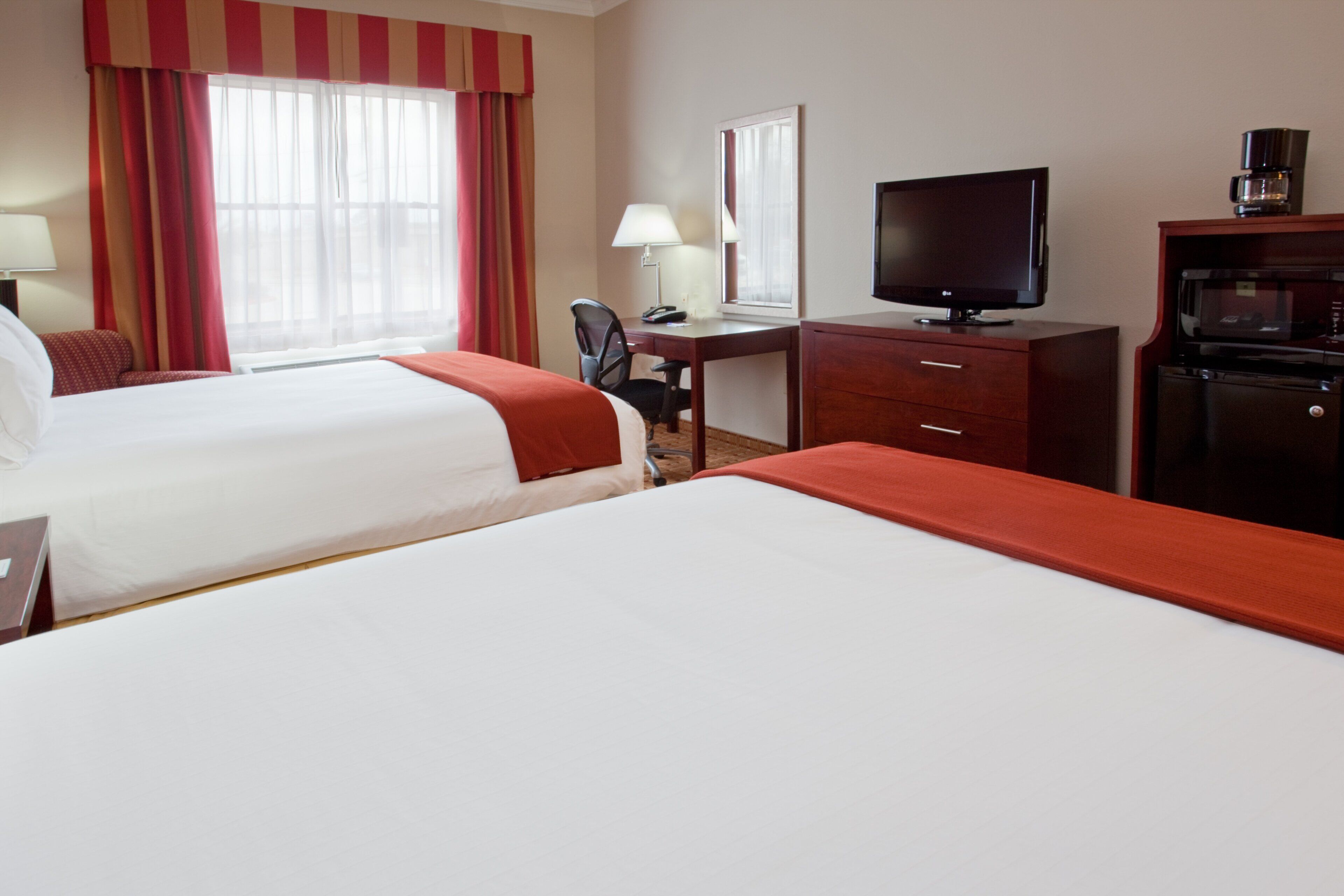 Ein Hotelzimmer mit zwei Betten, einem Schreibtisch mit Computer, einem Fernseher und einer Kaffeemaschine.