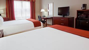 Una habitación de hotel con dos camas, un escritorio con computadora, televisión y cafetera.