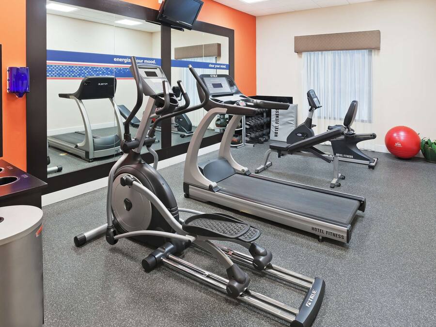 Un gimnasio de hotel con cintas de correr, máquinas elípticas y una pelota de ejercicios roja.