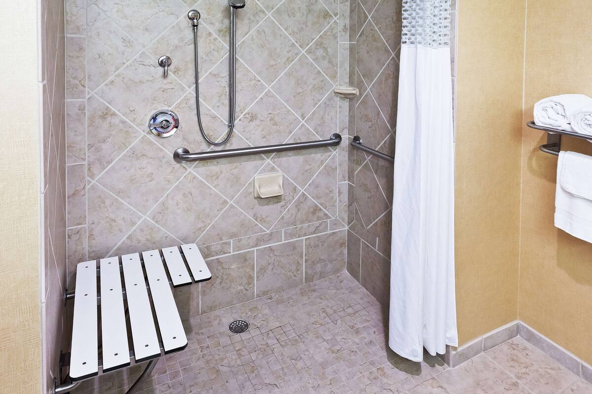 Un espace douche équipé d’une barre d’appui, d’un pommeau de douche à main, d’un robinet mural et d’un porte-serviettes avec des serviettes.