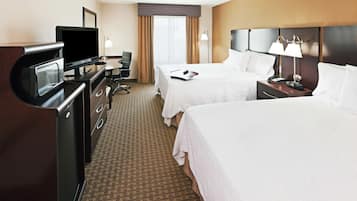 A hotel room with two beds, a desk with a television, a desk lamp, and a telephone.