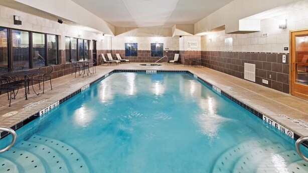 An indoor swimming pool with lounge chairs and tables, a tiled wall, and a door with a sign. - Hampton Inn and Suites Dumas (Dumas)