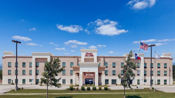 A Hampton Inn & Suites hotel with a brick facade, multiple windows, and a central entrance.
