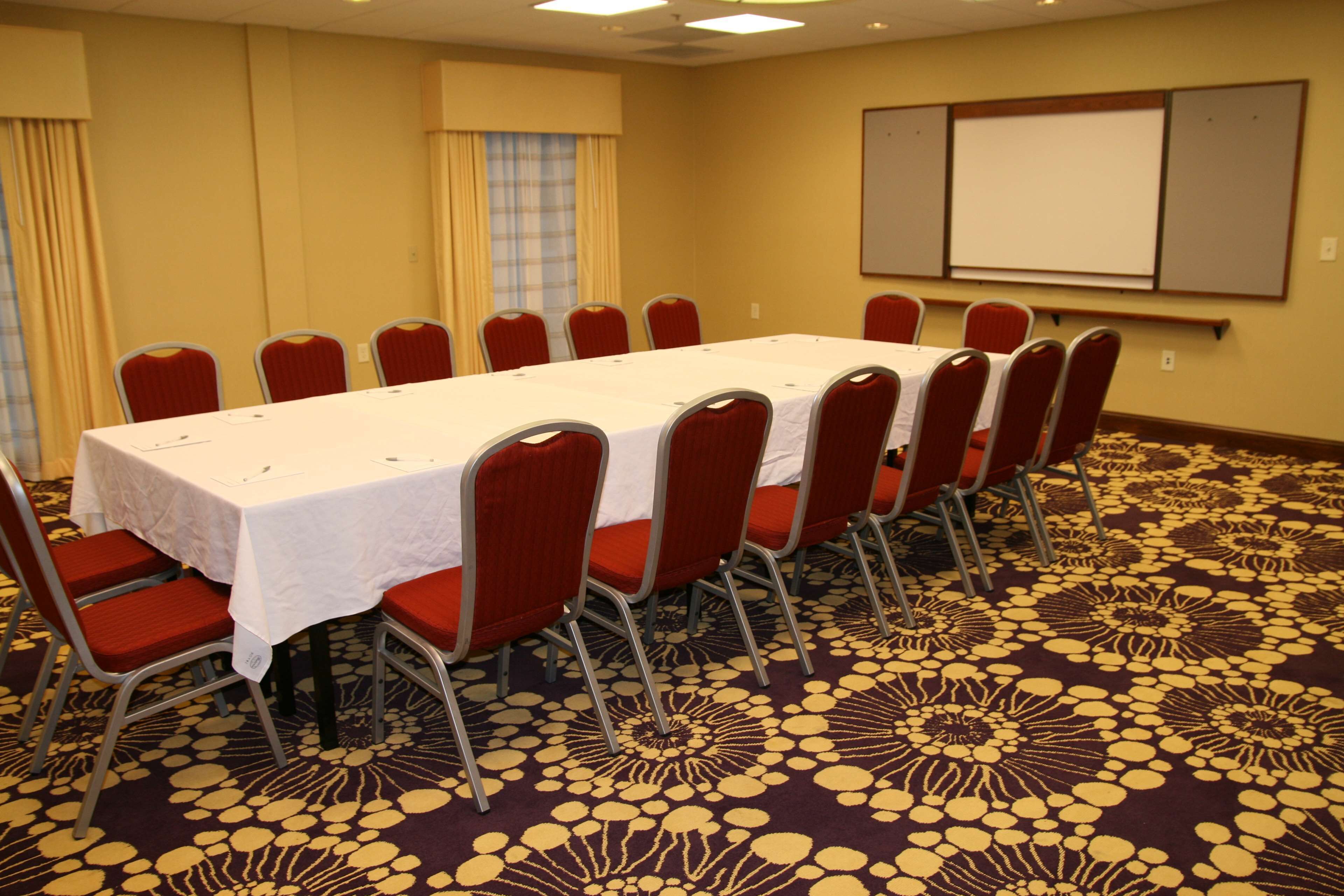 A conference room with a long table, red chairs, a white tablecloth, and a patterned carpet.