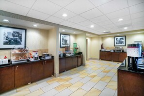 A hotel breakfast area with a buffet setup, including a coffee station and various food items.