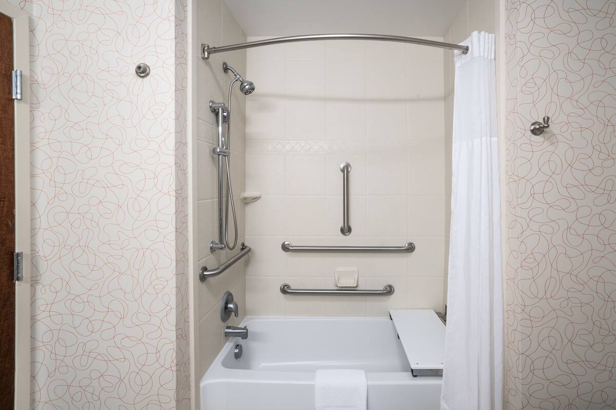 A bathroom with a bathtub, a shower with grab bars, and a toilet.