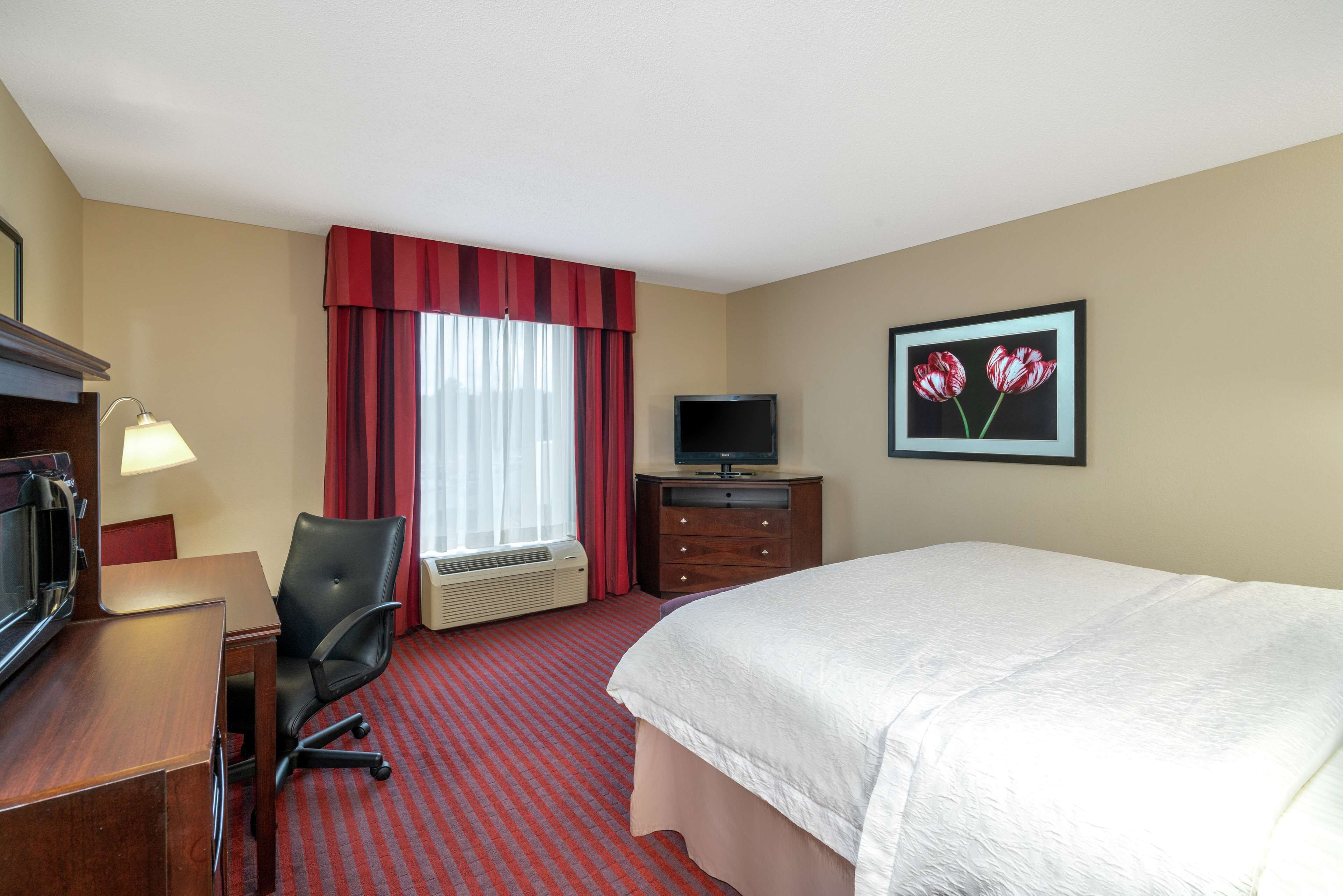 Habitación de hotel con cama, escritorio, silla, televisor y una pintura de tulipanes.