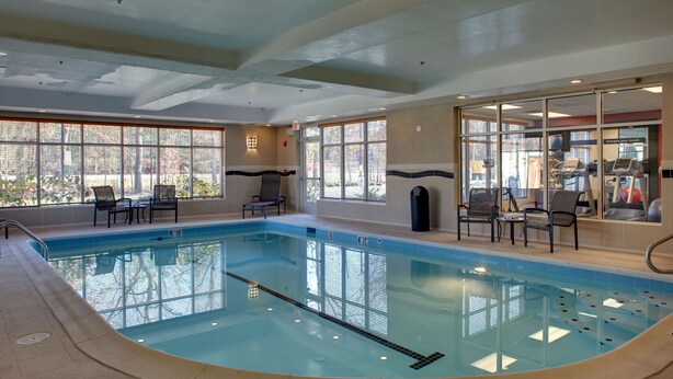 An indoor swimming pool with a clear view of the outside through large windows, a seating area with chairs, and exercise equipment. - Hampton Inn Richmond Airport (Sandston)