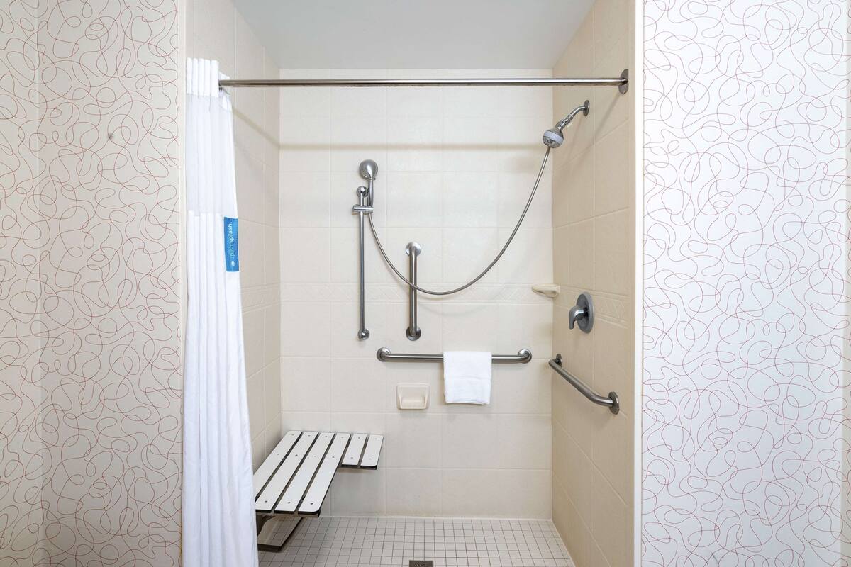 A shower with a grab bar, a bench, and a towel rack.