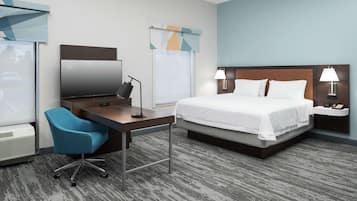 A hotel room with a bed, desk, chair, and a TV.