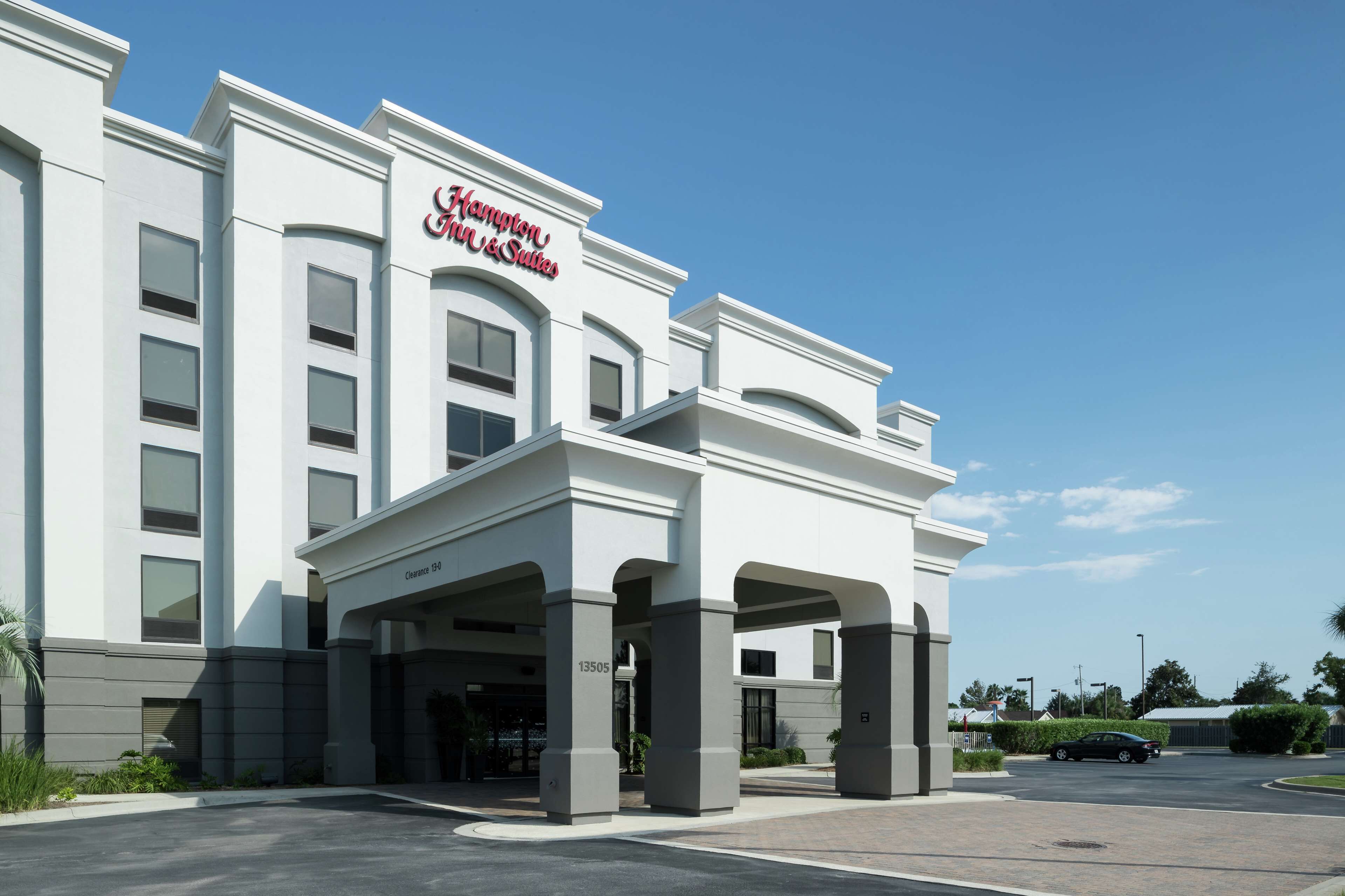 Un hotel con un cartel llamativo que dice "Hampton Inn & Suites" y un estacionamiento al frente.