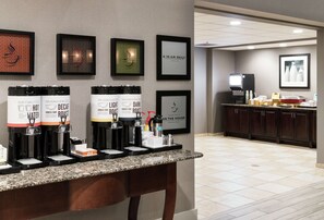 Angolo caffè con diverse macchinette per il caffè, un erogatore d'acqua e un menu incorniciato appeso al muro.