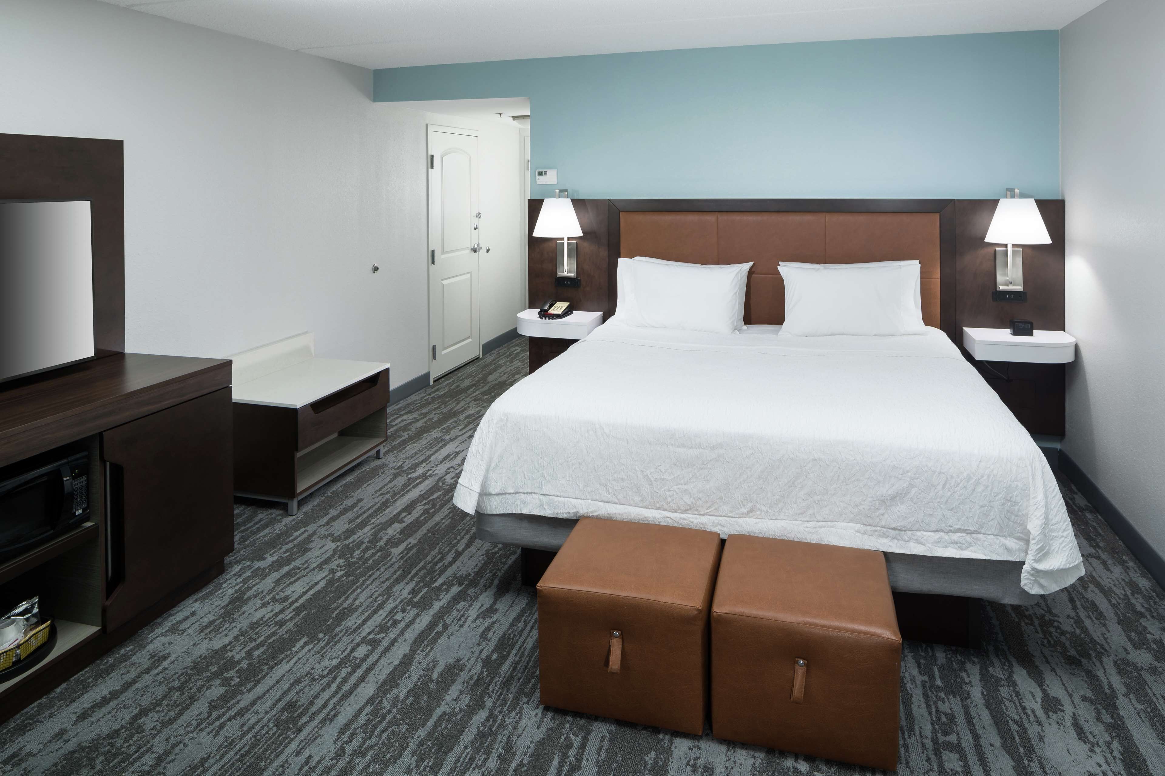 A hotel room with a large bed, two bedside tables with lamps, a small seating area, a television, and a door.