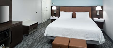 A hotel room with a large bed, two bedside tables with lamps, a small seating area, a television, and a door.