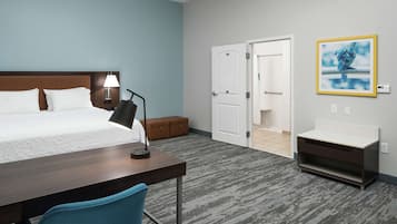 A hotel room with a bed, desk, chair, lamp, bedside table, and a bathroom visible through an open door.
