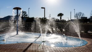 A water fountain with multiple jets, surrounded by a paved area and a metal fence. - Hampton Inn & Suites Panama City Beach-Pier Park Area (Panama City Beach)