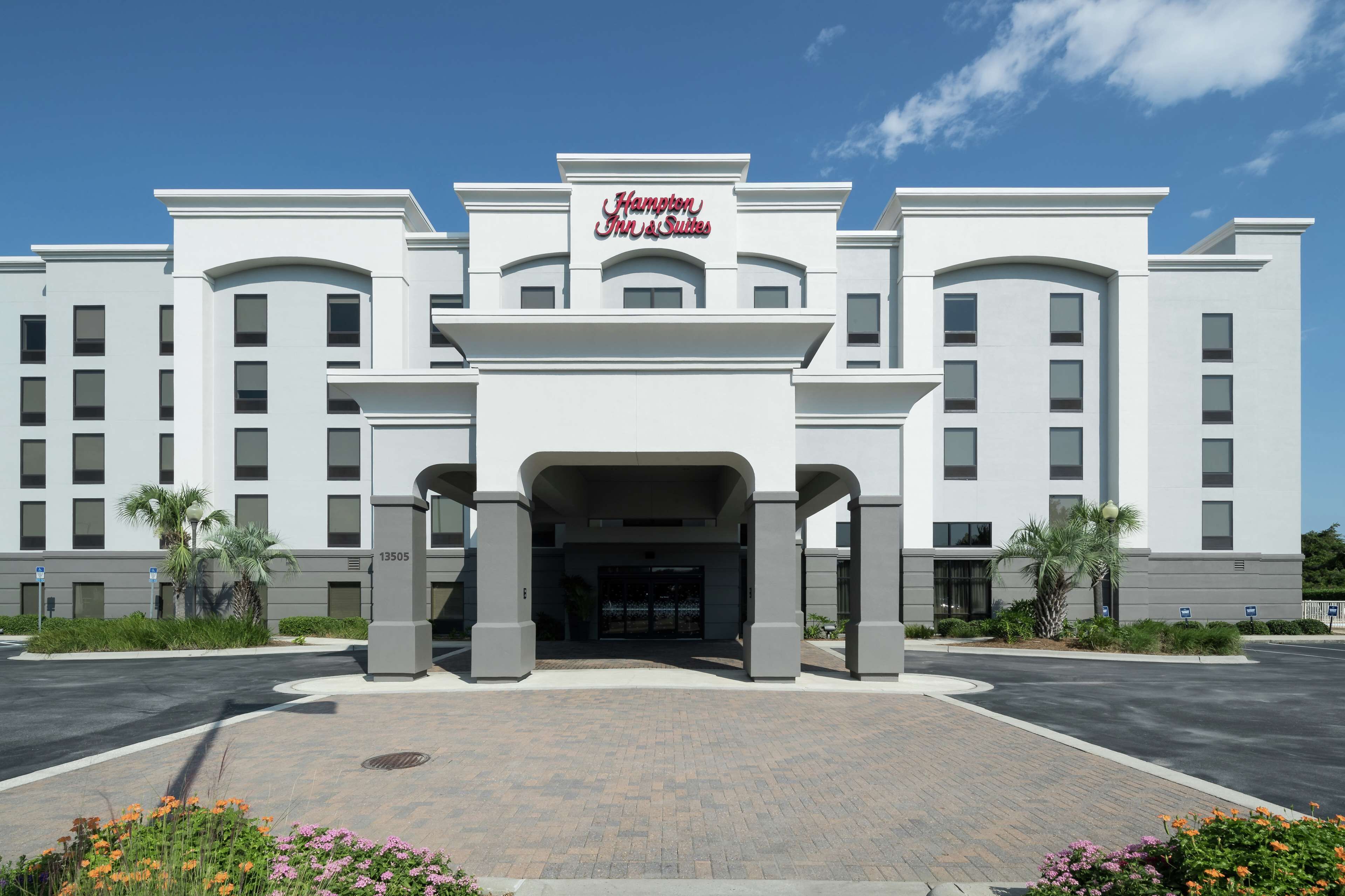 Un grand hôtel moderne, doté d’une entrée imposante et d’une enseigne indiquant « Hampton Inn & Suites ».