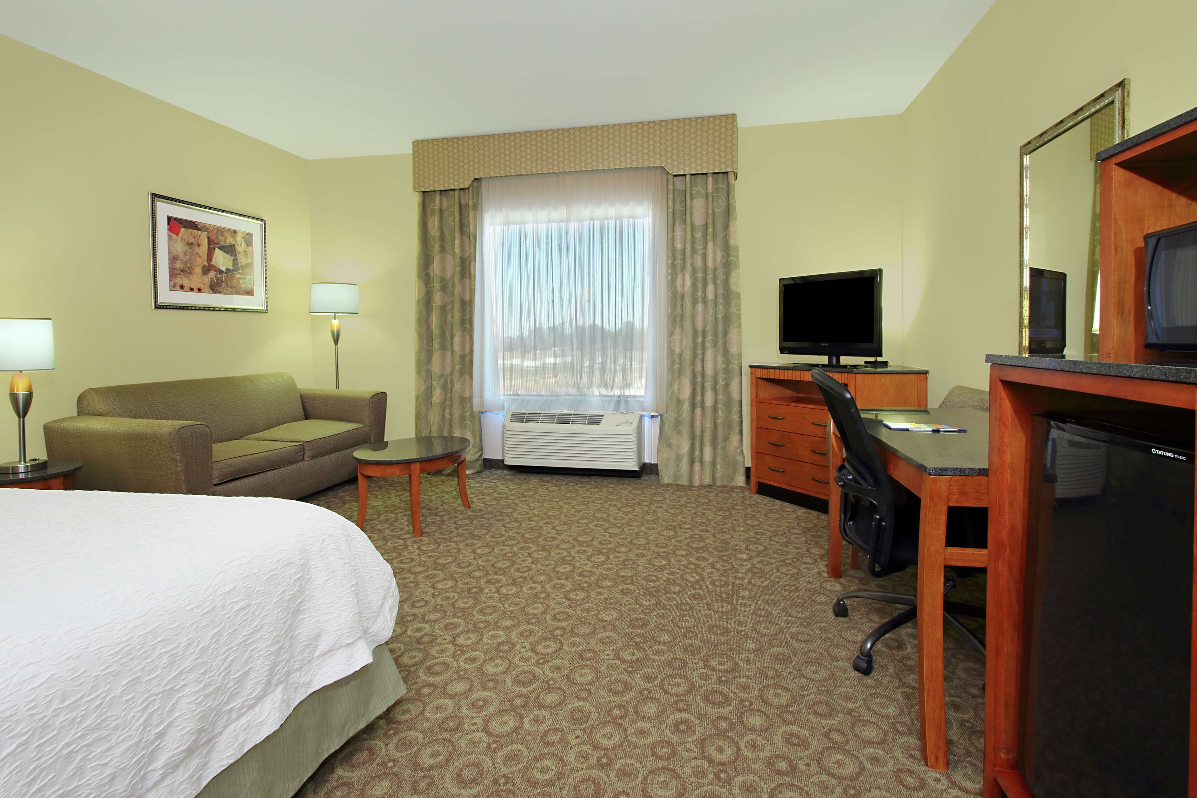 A hotel room with a bed, a desk, a chair, a television, and a window with curtains.