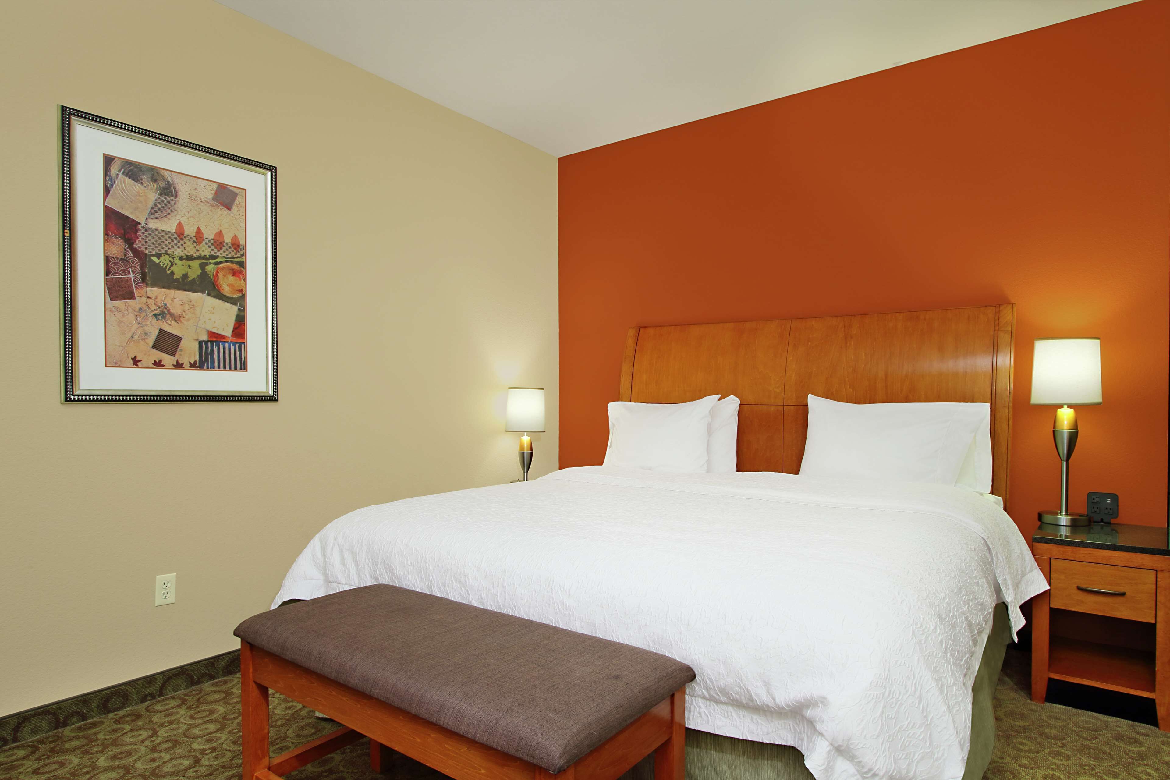 A hotel room with a large bed, two bedside lamps, a wooden bench, and a framed artwork on the wall.
