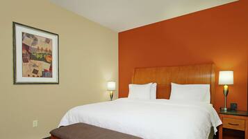 A hotel room with a large bed, two bedside lamps, a wooden bench, and a framed artwork on the wall.