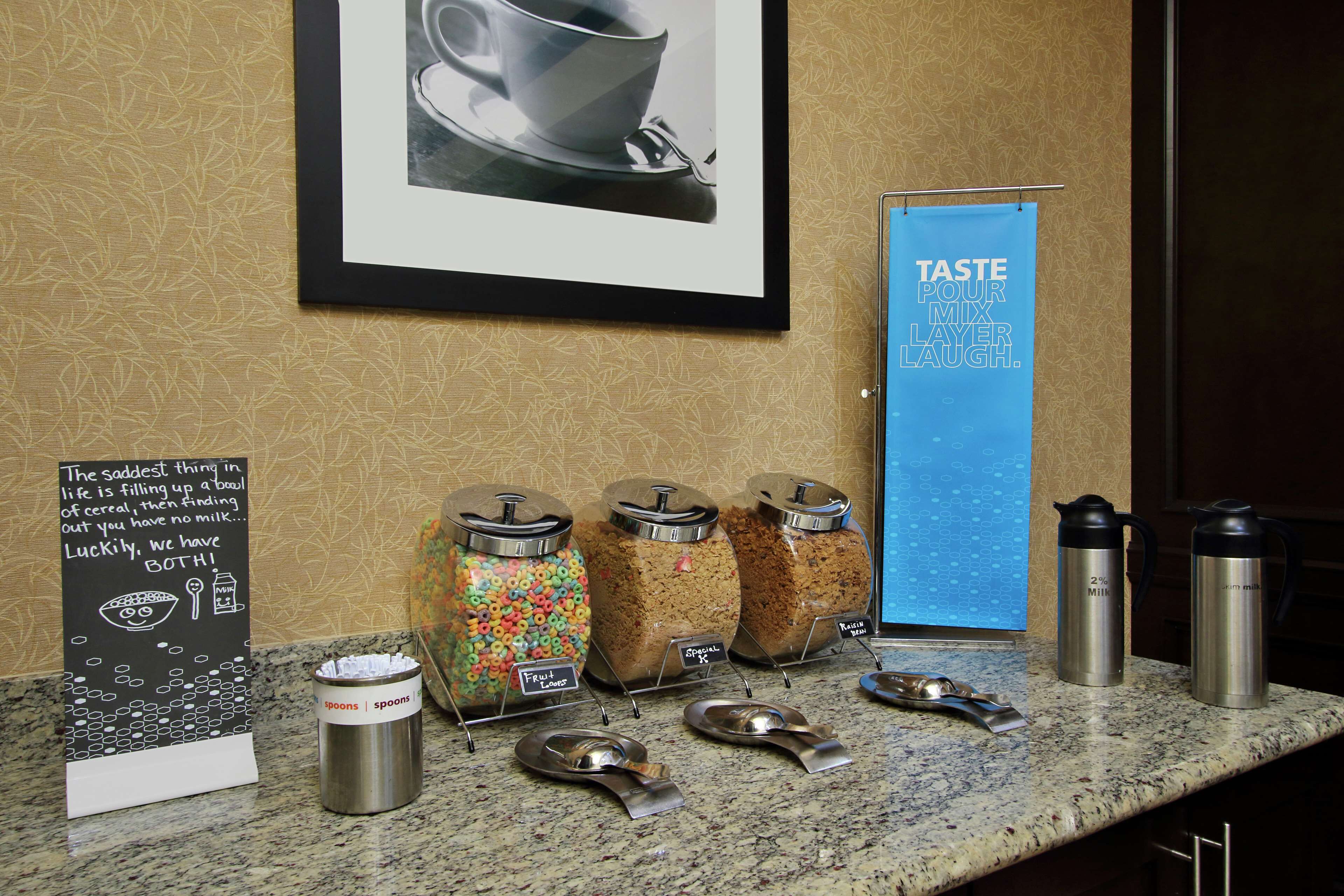 A hotel reception area with a coffee station, cereal dispensers, and a framed picture on the wall.