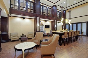 Un vestíbulo espacioso con techo alto, una zona de comedor con una mesa larga y sillas, y un área de estar con sofás y una mesa de centro.