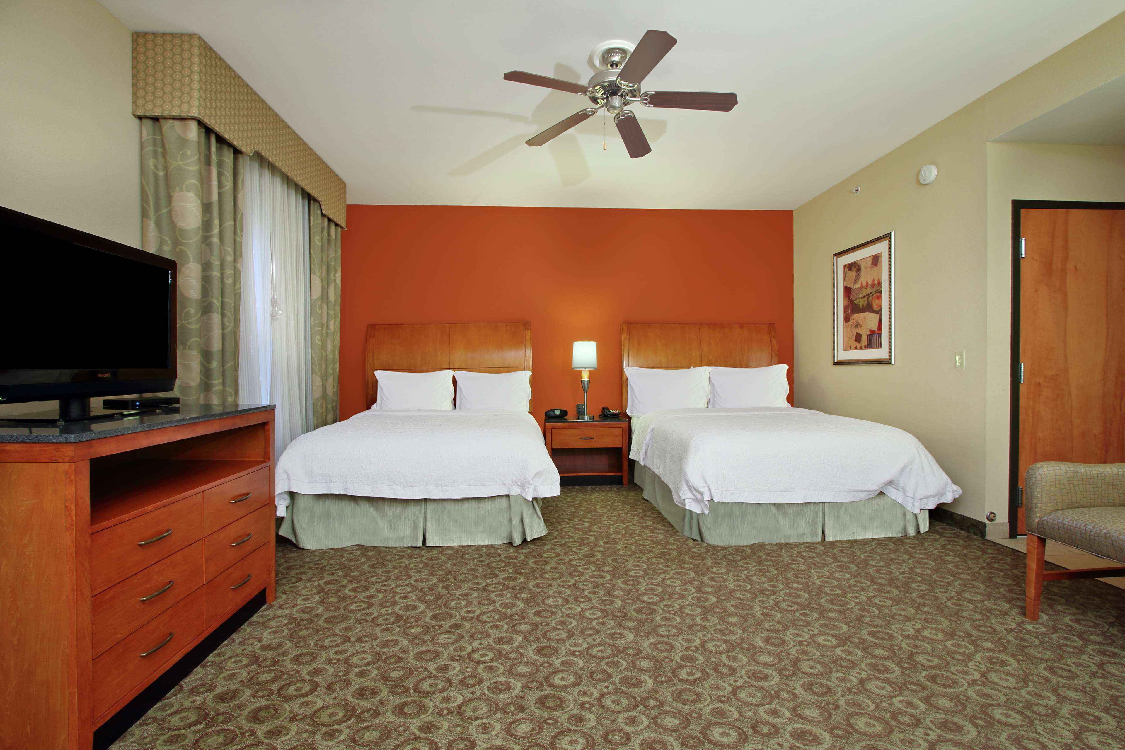 A hotel room with two beds, a TV, a ceiling fan, a nightstand, and a chair.