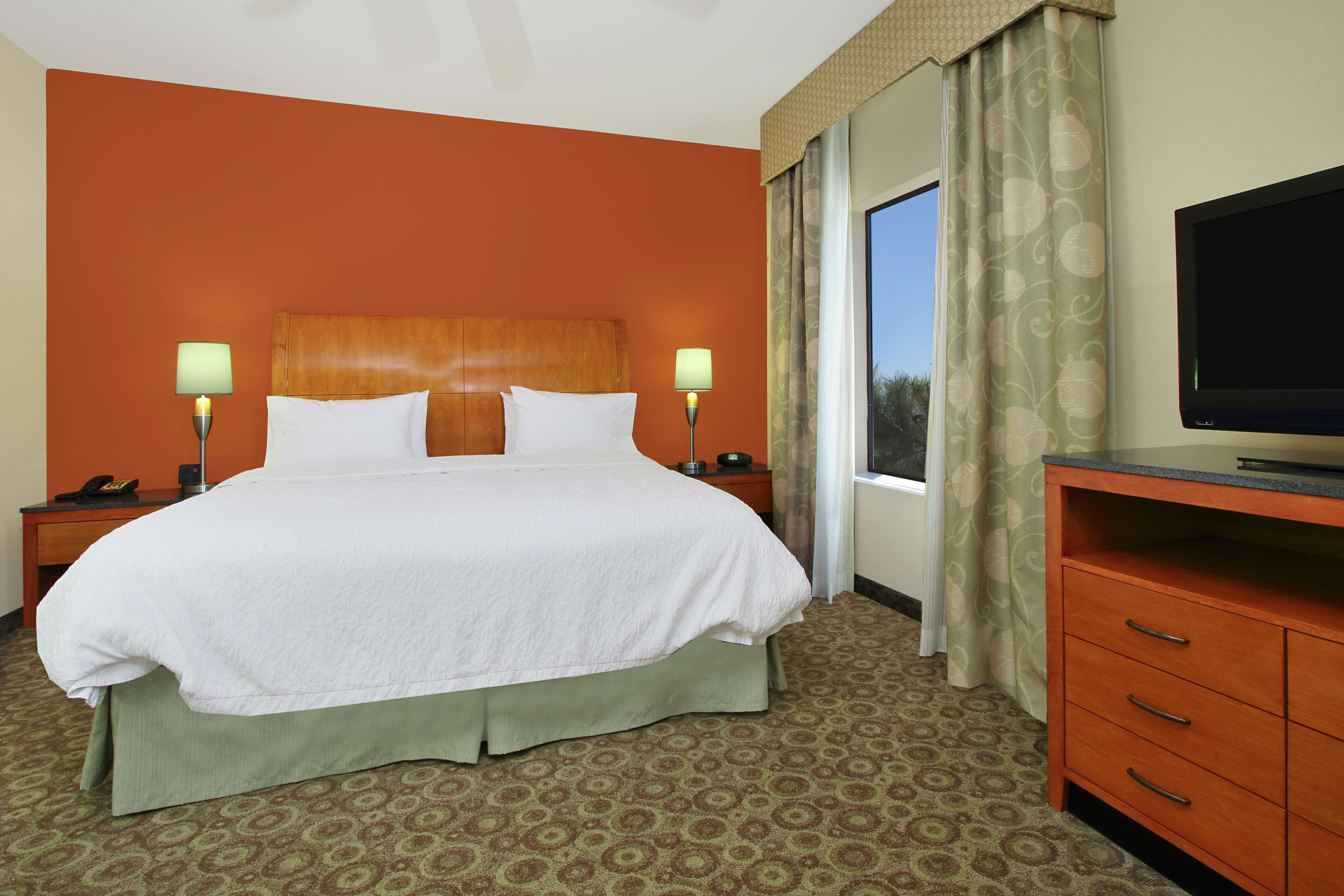 A hotel room with a large bed, two bedside lamps, a TV, and a window with curtains.