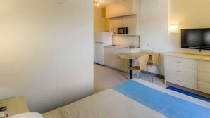 Habitación de hotel con cama, escritorio, silla, televisión y kitchenette.