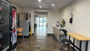 Un área de cocina limpia y moderna, con refrigerador, cafetera y una mesa de comedor con sillas.