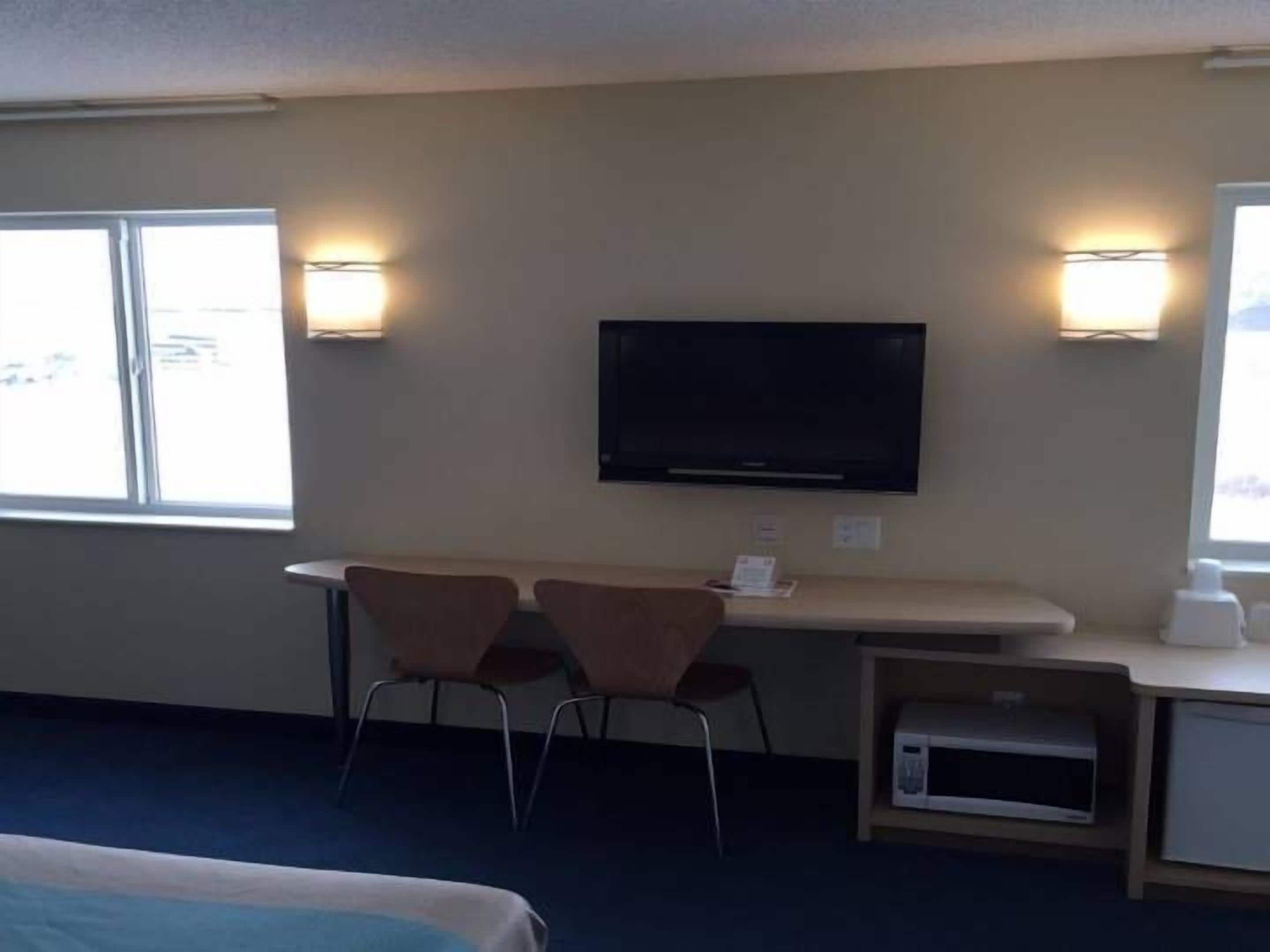 Ein Hotelzimmer mit einem Bett, einem Schreibtisch mit zwei Stühlen, einem Fernseher und zwei Wandleuchten.