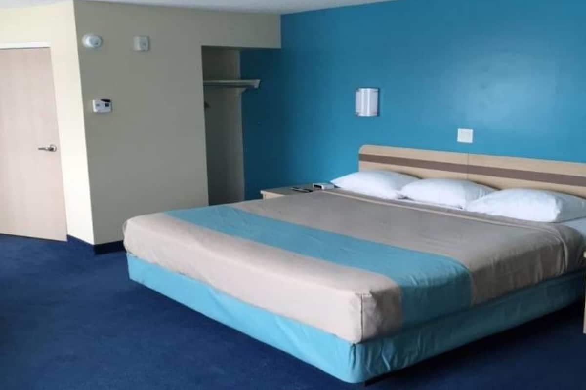 A hotel room with a bed, a nightstand, a wall-mounted lamp, and a door.